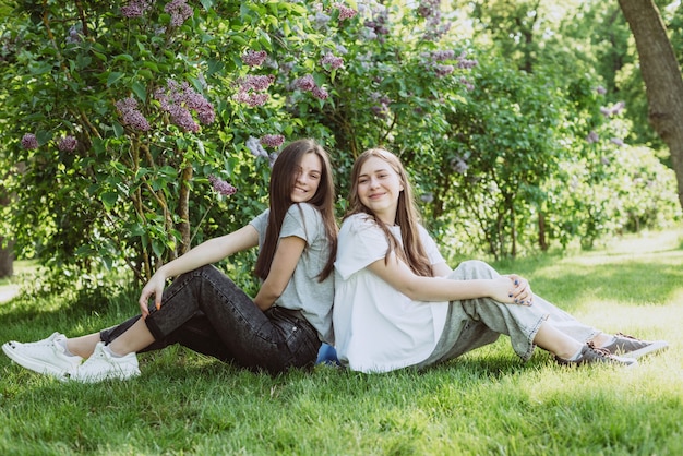 Twee jonge gelukkige tienermeisjes rusten in het park op het groene gras. Vrouwelijke vriendschap. Zachte selectieve focus.