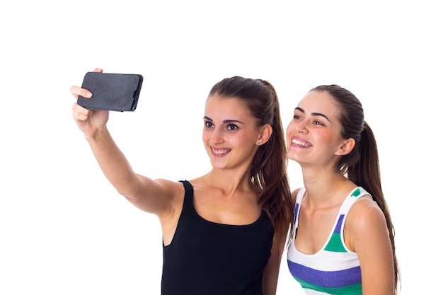 Twee jonge gelukkige vrouwen in gestreepte en zwarte overhemden maken selfie op witte achtergrond in studio