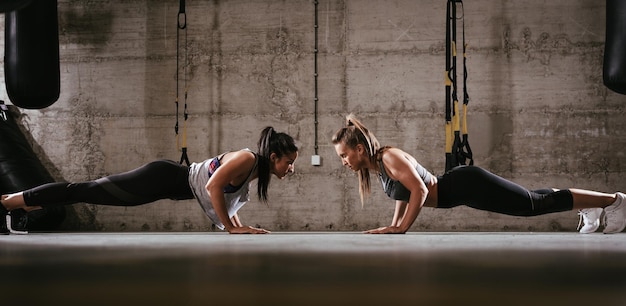 Twee jonge gespierde meisjes doen plank oefening bij de cross fit training.