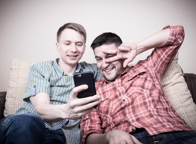 Twee jonge grappige jongens nemen selfie op smartphone zittend op de bank