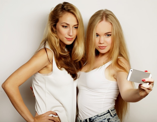 Twee jonge grappige vrouwen die selfie met mobiele telefoon nemen