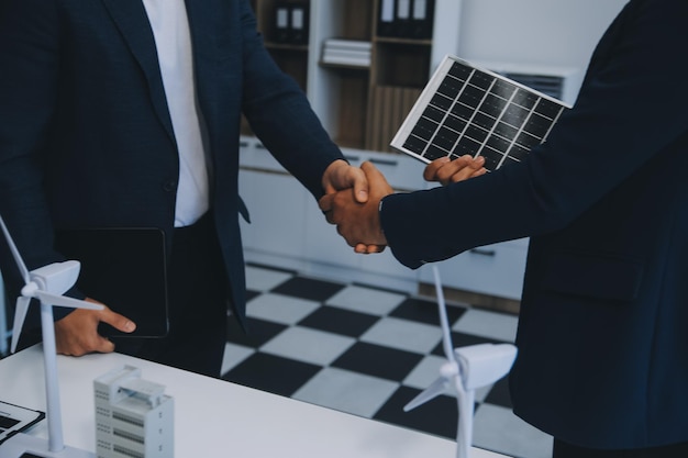 Foto twee jonge ingenieurs, deskundigen op het gebied van de installatie van zonnepanelen, vergaderden en bespraken de werkzaamheden met betrekking tot de planning van het installeren van zonne-photovoltaïsche panelen op het dak van de kantoorkamer met een fabrieksbouwplan.