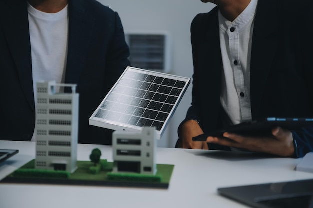 Twee jonge ingenieurs, deskundigen op het gebied van de installatie van zonnepanelen, vergaderden en bespraken de werkzaamheden met betrekking tot de planning van het installeren van zonne-photovoltaïsche panelen op het dak van de kantoorkamer met een fabrieksbouwplan.