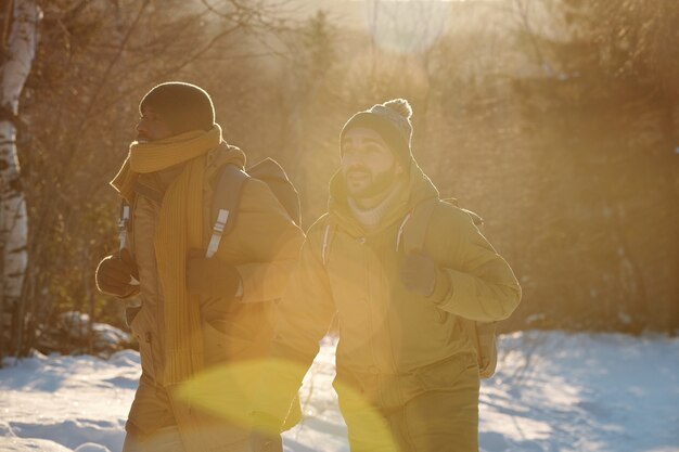 Twee jonge interculturele backpackers die zich door het winterbos bewegen