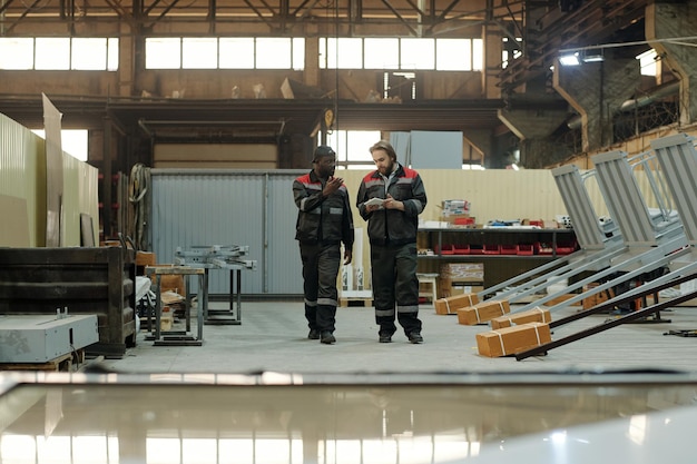 Twee jonge interculturele mannelijke fabrieksarbeiders die onderweg in gesprek zijn