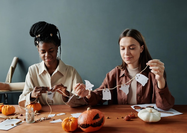 Twee jonge interculturele vrouwen maken halloween decoratie met geesten