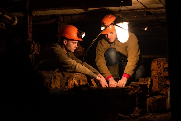 Twee jonge jongens in een werkend uniform en beschermende helmen, zittend in een lage tunnel. mijnwerkers