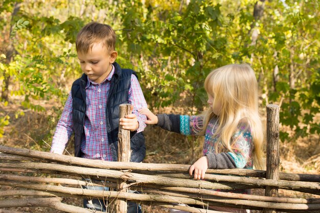 Twee jonge kinderen spelen bij een rustieke houten omheining van verweven takken met het kleine meisje dat uitreikt om de arm van de jongen aan te raken