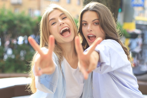 Twee jonge lachende hipster vrouwen in zomer kleding poseren op straat. Vrouw positieve gezicht emoties tonen.