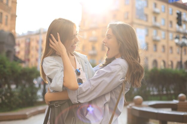 Twee jonge lachende hipster vrouwen in zomer kleding poseren op straat. Vrouw positieve gezicht emoties tonen.