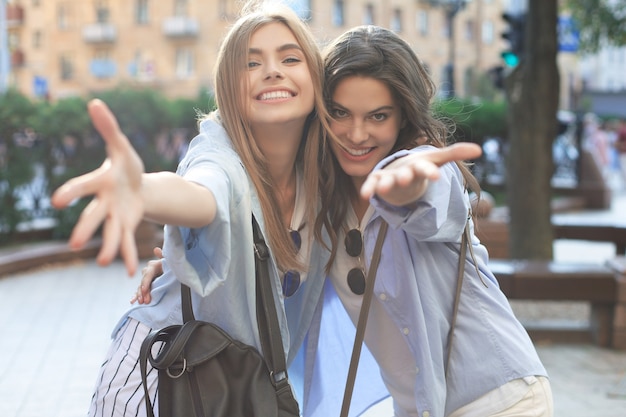 Twee jonge lachende hipster vrouwen in zomer kleding poseren op straat. Vrouw positieve gezicht emoties tonen.