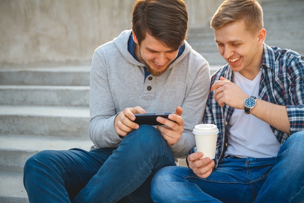 Twee jonge lachende mannen kijken naar een video op een smartphone