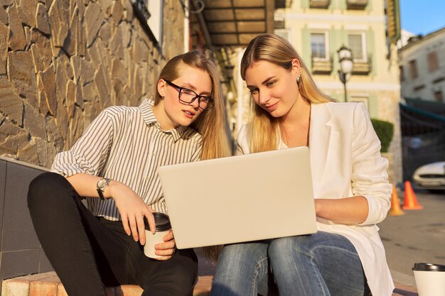 Twee jonge lachende vrouwen kijken naar laptopmonitor die buiten zit