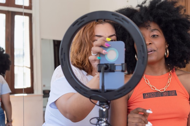 Twee jonge Latijnse meisjes maken een video voor de sociale netwerken met hun telefoon en een lichtring