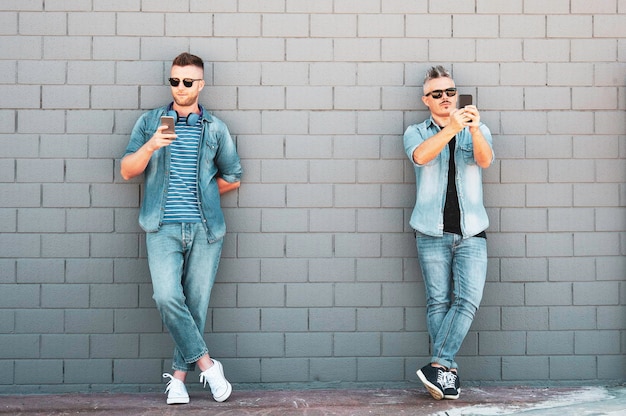 Twee jonge mannen die naar een mobiele telefoon kijken, leunen tegen de muur. Een paar coole jongens die een smartphone gebruiken die buiten op straat staat