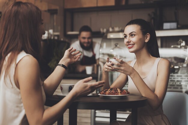 Twee jonge meisjes communiceren in een café aan de tafel