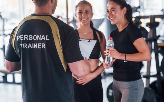 Twee jonge meisjes in sportieve kleding zijn overdag samen in de sportschool met hun mannelijke personal trainer.