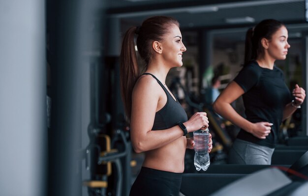 Twee jonge meisjes in sportieve kleding zijn samen in de sportschool op de loopband.