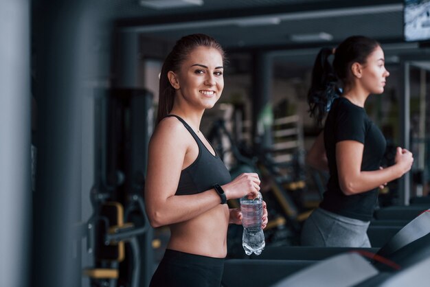 Twee jonge meisjes in sportieve kleding zijn samen in de sportschool op de loopband.