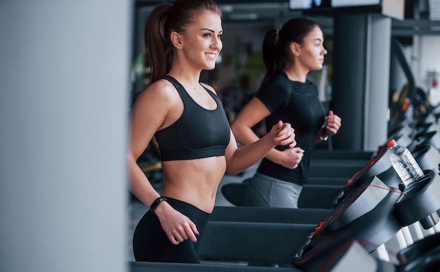 Twee jonge meisjes in sportieve kleding zijn samen in de sportschool op de loopband.