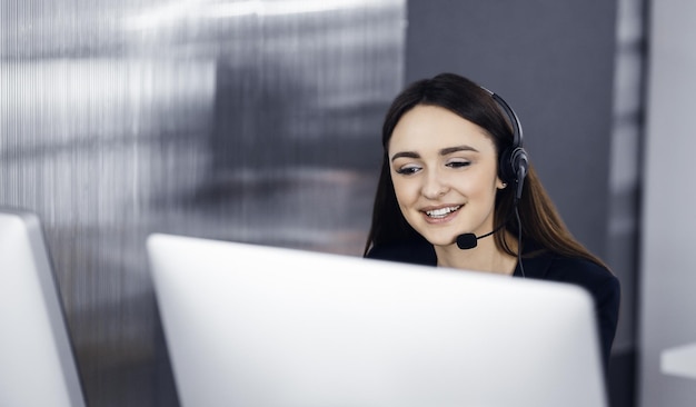 Twee jonge mensen in headsets glimlachen en praten met de klanten terwijl ze aan het bureau zitten in een modern kantoor Callcenteroperators aan het werk