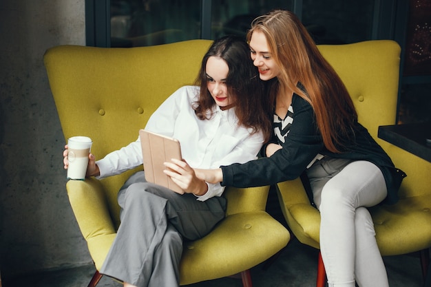 Twee jonge modieuze onderneemsters die in een koffie zitten en de tablet gebruiken