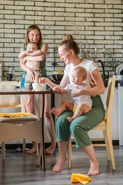 Twee jonge moeders geven samen hun gelukkige baby's melkpap in de keuken