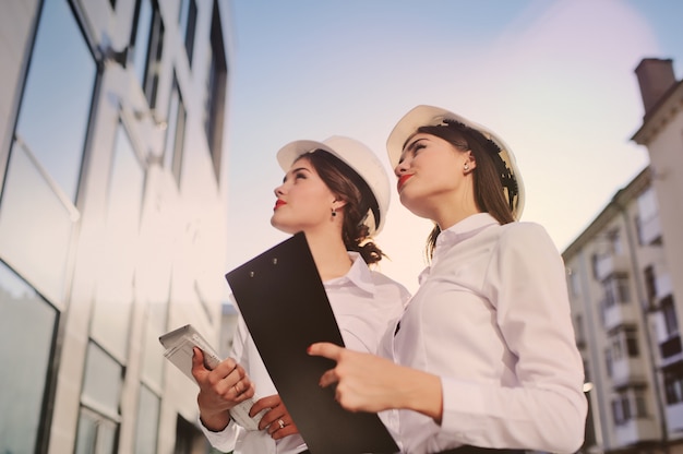 Twee jonge mooie bedrijfsvrouwen industriële ingenieurs in bouwhelmen