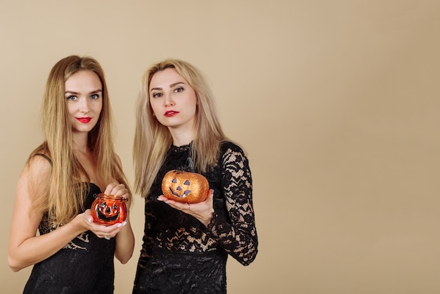 Twee jonge mooie blondines houden pompoenvormige snoepmanden op een beige achtergrond. Halloween en reclame concept.