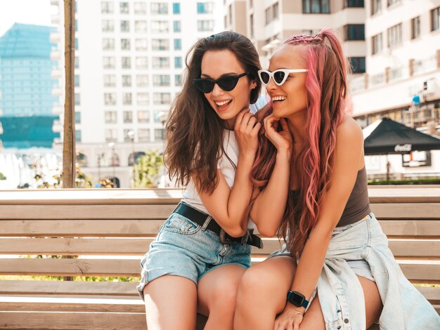 Twee jonge mooie lachende hipster vrouw in trendy zomerkleren. Sexy zorgeloze vrouwen poseren in de straat met roze haren. Positieve pure modellen die plezier hebben bij zonsondergang. Vrolijk en gelukkig