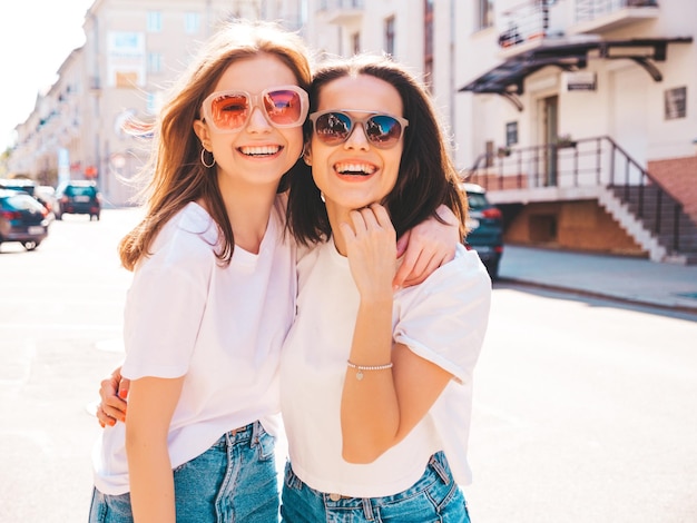 Twee jonge mooie lachende hipster vrouw in trendy zomerkleren. Sexy zorgeloze vrouwen poseren in de straat. Positieve pure modellen die plezier hebben bij zonsondergang, knuffelen en gek worden. Blij en vrolijk