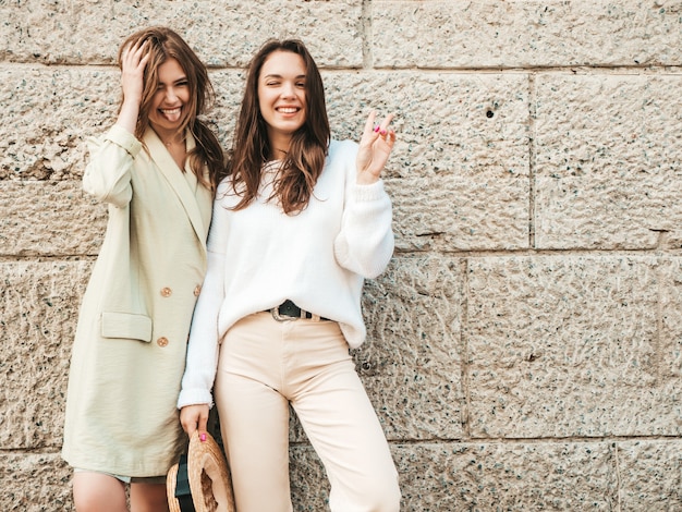 Twee jonge mooie lachende hipster-vrouwen in trendy witte trui en jas