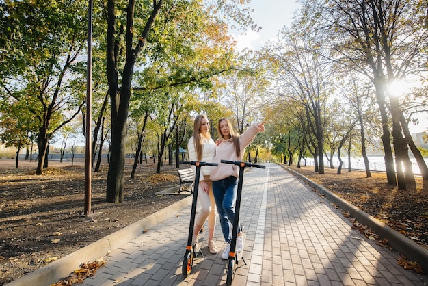 Twee jonge mooie meisjes rijden elektrische scooters in het Park op een warme herfstdag.
