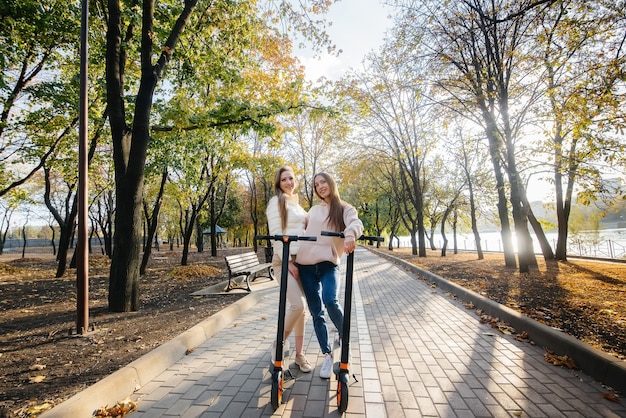 Twee jonge mooie meisjes rijden elektrische scooters in het Park op een warme herfstdag