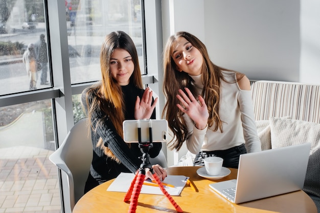 Foto twee jonge mooie meisjes zitten in een café, nemen videoblogs op en communiceren op sociale netwerken.