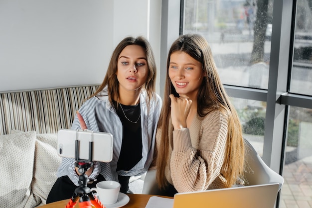 Twee jonge mooie meisjes zitten in een café, nemen videoblogs op en communiceren op sociale netwerken.