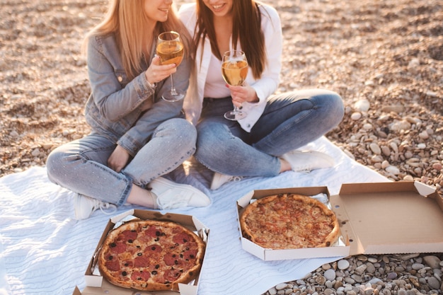 Twee jonge mooie vriendinnen die plezier hebben met pizza en wijn op het strand
