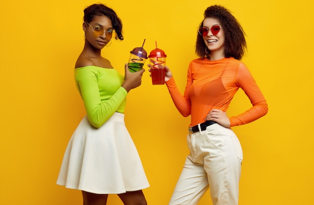 Twee jonge mooie vrouwen in kleurrijke zomer kleding met cocktails