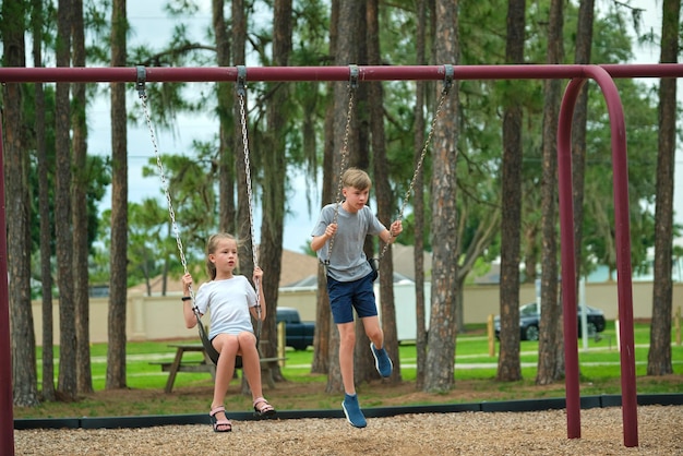 Twee jonge tienerkinderen, meisje en jongen die samen buiten op schommels spelen op een zonnige vakantiedag