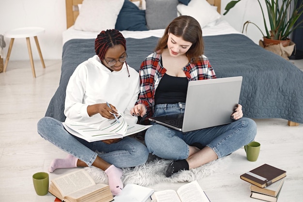 Twee jonge tienermeisjes zittend op een vloer in de buurt van bed studeren en gebruiken een laptop