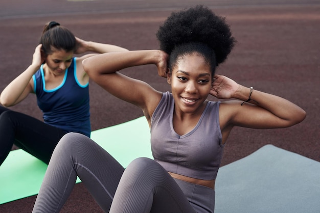 Twee jonge verschillende vrouwen gaan sporten buiten in het stadion ab crunches