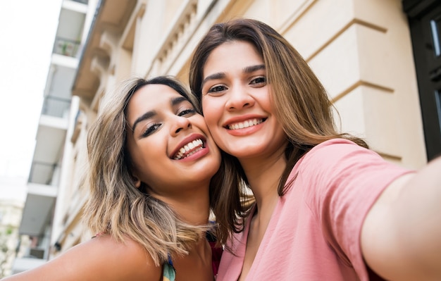 Twee jonge vrienden glimlachen en nemen samen een selfie terwijl ze buiten staan. stedelijk concept.