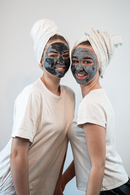 Twee jonge vrienden of zussen die een klei gezichtsmasker aanbrengen geïsoleerd op wit Blijf mooie anti-veroudering behandeling Pure schoonheid