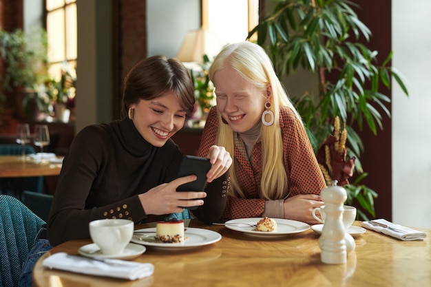 Twee jonge vrolijke vriendinnen bespreken online foto of video in mobiele telefoon
