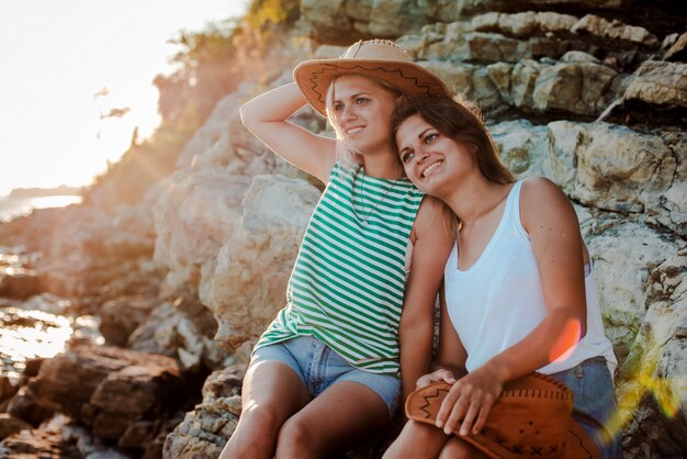 Twee jonge vrolijke vrouwen in hipsters hoeden op een rots aan de kust van de zee.