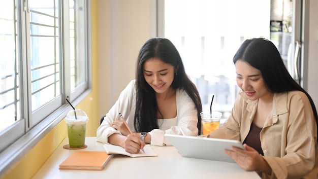 Twee jonge vrouw die digitale tablet gebruikt en hun project bespreekt in café.