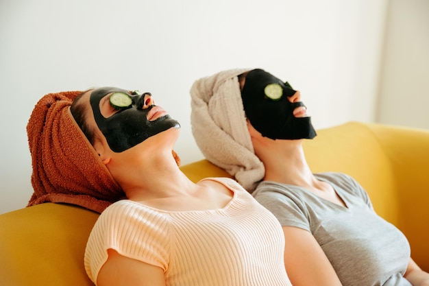 Twee jonge vrouw liggend met cosmetische maskers op hun gezicht en plakjes komkommer op hun ogen zijaanzicht...