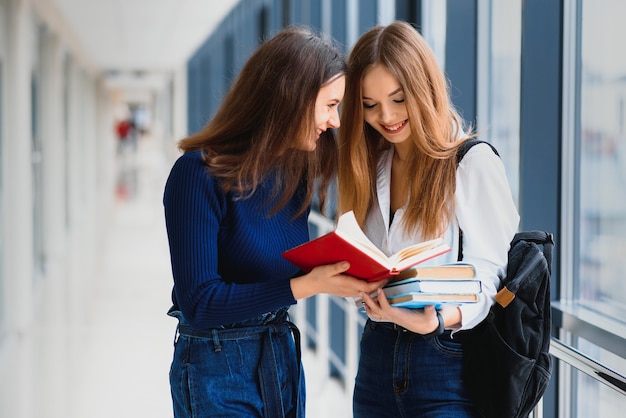 Twee jonge vrouwelijke studenten staan met boeken en tassen in de gang