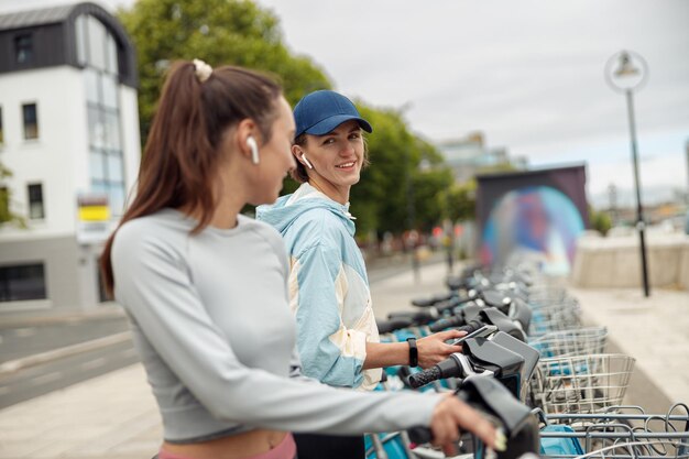 Twee jonge vrouwelijke vrienden die een fiets huren in de stadsdienst voor het delen van fietsen om te wandelen