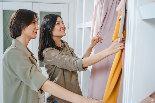 Twee jonge vrouwelijke vrienden die een jurk kiezen in een winkel of kleedkamer Winkelmode en vriendschapsconcept